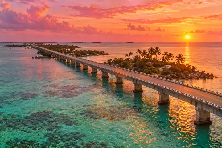 A long two-lane bridge across turquoise shallow water in the Florida Keys at sunset
